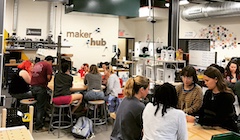 A classroom lab with students working at tables with the sign "maker hub" in the background.