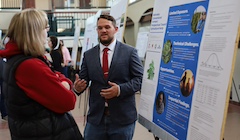A student presents his poster to an audience at a poster fair.